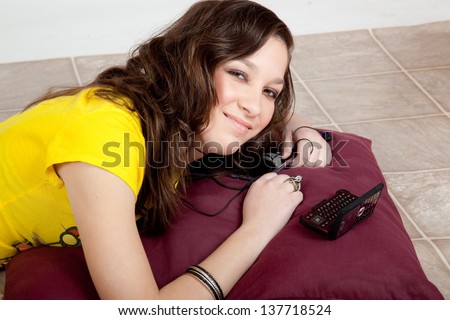 Pretty teenage girl in yellow shirt, reclining and listening to her music and smiling at the camera with happiness