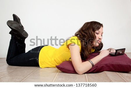 Pretty teenage girl in yellow shirt, reclining and listening to her music and looking at the her music with  thoughtfulness