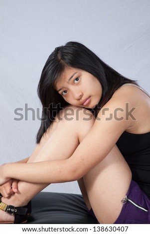 Pretty Asian woman sitting in tank top  and looking at the camera with her cheek on her knees