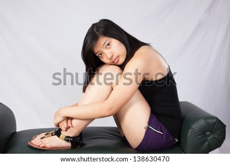 Pretty Asian woman sitting in tank top  and looking at the camera with her cheek on her knees