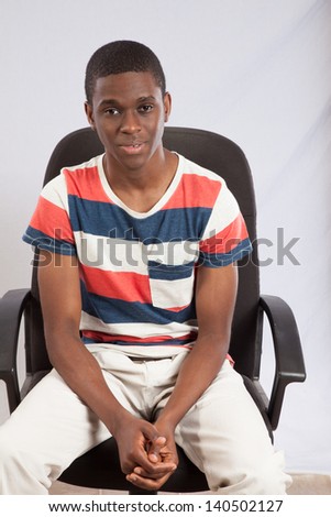 Handsome black man in striped shirt sitting in a chair for a desk, looking at the camera with a thoughtful expression and arms crossed