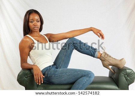 Lovely black woman in white tank top and blue jeans, sitting casually on a bench and looking at the camera