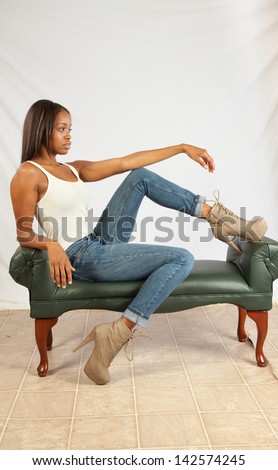Lovely black woman in white tank top and blue jeans, sitting casually on a bench and looking to the right