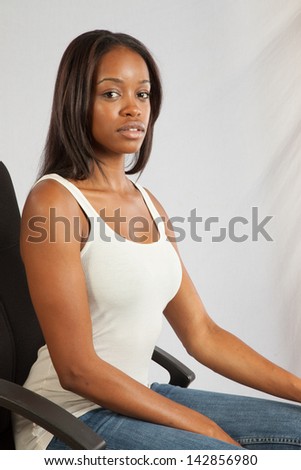 Lovely black woman in a white, tank top, sitting in a executive chair, and looking at the camera with a calm, but serious, pensive  expression