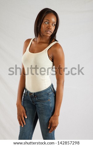 Lovely black woman in a white, tank top, sitting and holding her left arm with her right hand, while she looks down thoughtfully
