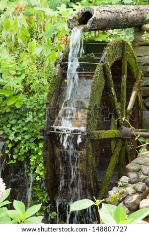 Rock City, Lookout Mountain, Tennessee, USA, water from a broken pipe spilling on an old mill wheel, surrounded by bushes and green growth