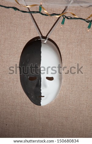 Party mask, painted black and white, hanging from colored lights