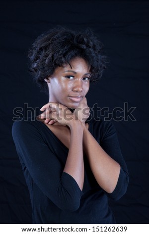 Thoughtful black woman wearing a black shirt shirt,  looking at the camera with both hands under her chin, and with a black background