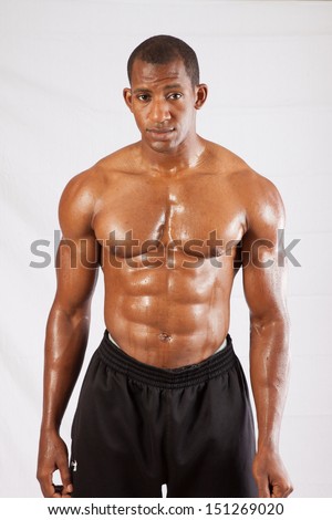 Muscular black man shirtless with his chest, abdomen and arms glistening with sweat,