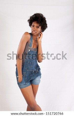 Lovely black woman in blue jean overall shorts, standing and looking seriously arms stretched over her head