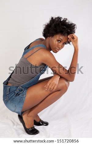 Lovely black woman in blue jean overall shorts, standing and looking seriously arms stretched over her head