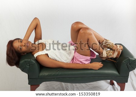 Thoughtful, black woman reclining on a bench with her hand behind her head and a thoughtful look