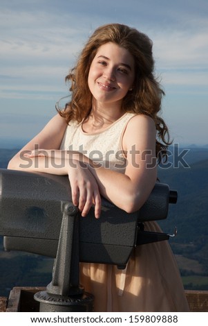 Pretty Caucasian woman standing with a viewer at a mountain overlook and looking at the camera with a friendly, happy, smile