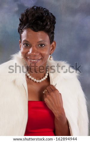 Pretty black woman  in a red sleeveless dress and white fur jacket, looking  at the camera  with a bright, happy smile