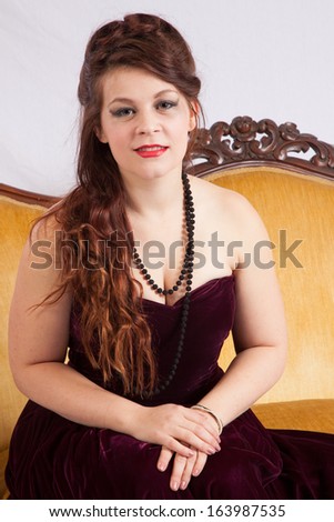 Pretty Caucasian woman in a short red dress, sitting on an old couch and looking with a relaxed flirting expression