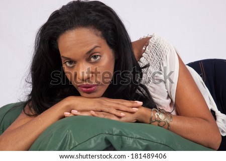 Pretty Black woman laying on a couch, looking at the camera with a friendly, thoughtful expression
