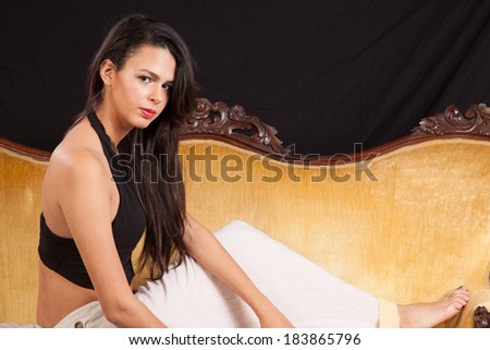 Pretty Caucasian woman sitting on a gold couch and looking at the camera with a serious but friendly expression