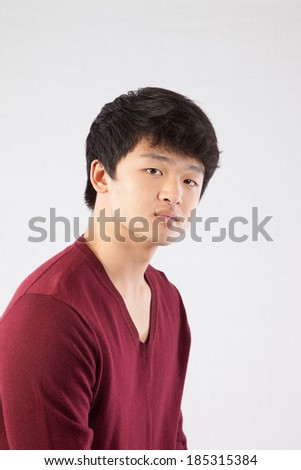 Cute South East Asian teenager in a red sweater,  looking  at the camera with a serious expression.