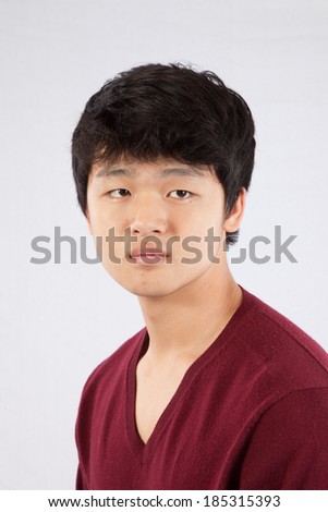 Cute South East Asian teenager in a red sweater,   looking to the right with a serious expression.
