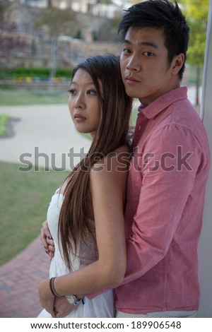 East Asian couple, man and woman outdoors standing with her back to his chest, and looking at the camera