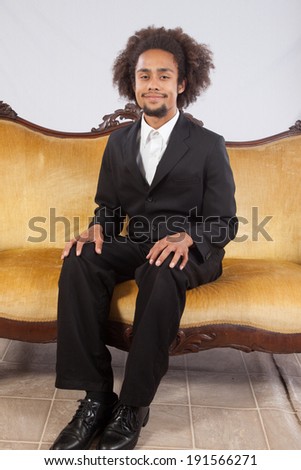 Handsome black man in suit, sitting on a gold couch and looking at the camera