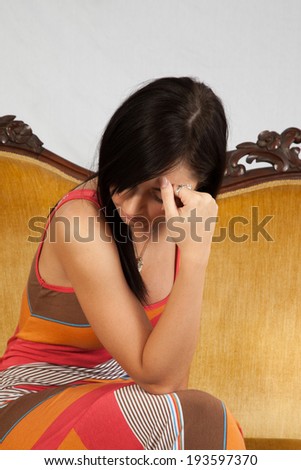 Pretty woman sitting on gold couch with chin on hand looking down in a gloom