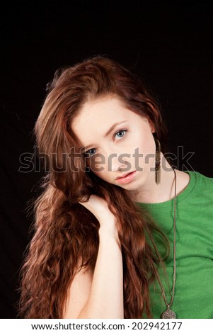 Pretty woman in green blouse, with long hair, with one hand in her hair, looking at the camera thoughtfully