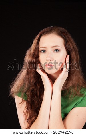 Pretty woman in green blouse, with long hair, with hands on her face, looking at the camera,