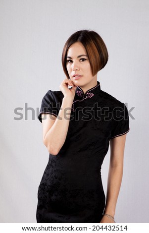 Pretty woman with short hair and wearing a black Asian blouse, looking at the camera with a thoughtful expression and her hand on her chin