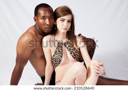 Mixed race couple sitting together, he is topless and she is wearing a leopard print bathing suit,