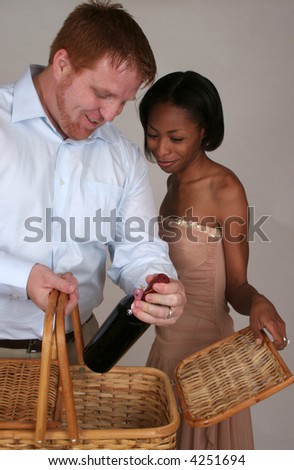 African American woman and white man, a mixed couple   together with a pick-nick basket and a bottle of wine.