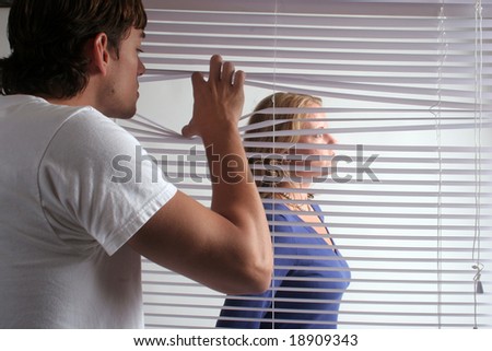 A mam peeks through the blinds at a woman