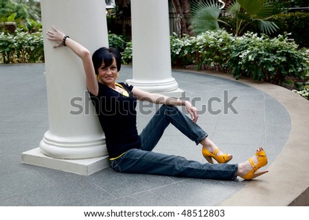 Woman sitting against white column in a playful and sexy mood