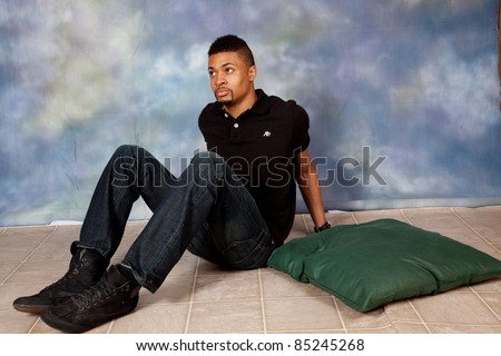 Handsome black man sitting on the floor and thinking with a serious expression