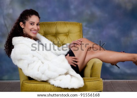 Pretty caucasian woman sitting sideways in a chair with her legs over the armrest and  a  big smile and eye contact