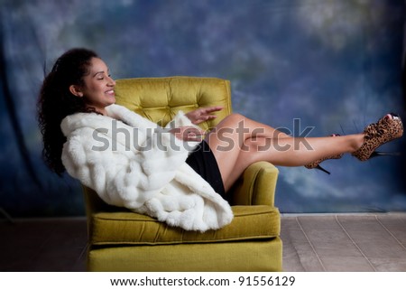 Pretty caucasian woman sitting sideways in a chair with her legs over the armrest and  a  big smile