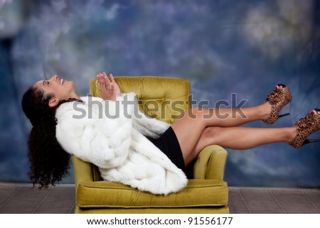 Pretty caucasian woman sitting sideways in a chair with her legs over the armrest and  a  big laugh