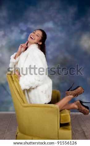 Pretty Caucasian woman kneeling backwards in a chair and laughing with her head thrown back.