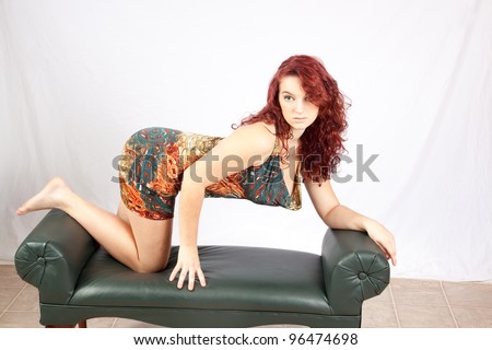 Pretty redhead teenage girl kneeling on a bench and leaning on her elbows, looking wistfully back over her shoulder