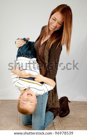 A mother laughing and playing with her young son as she holds him upside down