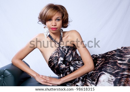 Pretty African American woman in a lovely formal dress with bare shoulders,   looking at the camera while leaning to her right