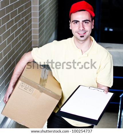 Smiling young courier with package and blank clipboard
