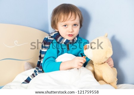 Little sick baby boy checking teddy bear\'s body temperature in bed