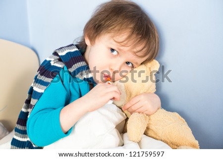 Sick little boy checking his body temperature and holding teddy bear