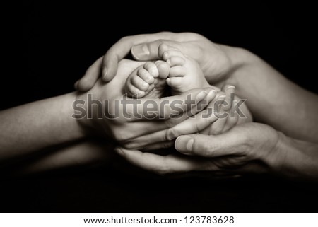Parents holding their child\'s feet gently - black and white photograph