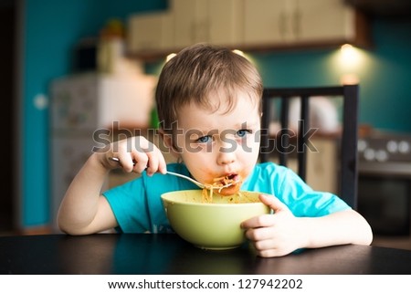 Boy is eating spaghetti with souce on his face