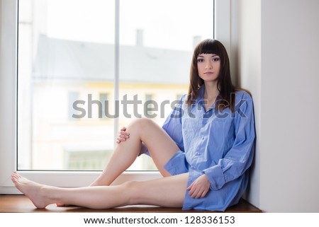 Portrait of beauty brunette sitting on window sill at the morning