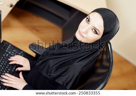 Muslim woman sitting on an office chair and working on the computer in the office. Overhead