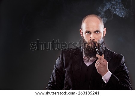 Portrait of  bald bearded man wearing old-fashioned suit and smoking a pipe. A lot of smoke in the picture. Photo taken in the studio on a gray background