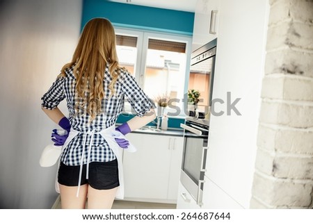 back view of young woman getting ready for kitchen cleaning. On her hands protective rubber gloves. Holding a bottle with detergent